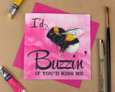 Greetings card with the words 'I'd be buzzin' if you'd kiss me' with the word 'be' replaced with an illustrated bumblebee on pink watercolour background