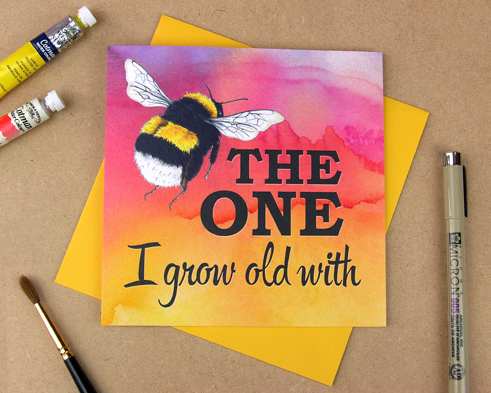 Greetings card with the words 'Be the one I grow old with' with the word 'be' replaced with an illustrated bumblebee on multi-coloured watercolour background