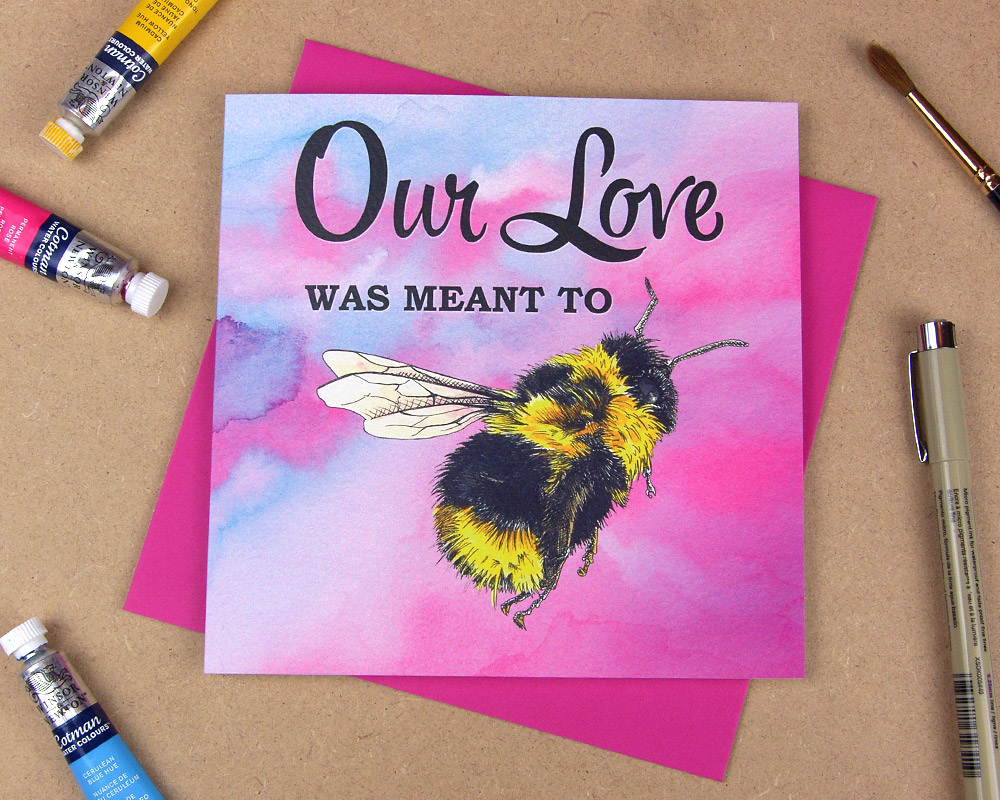 Greetings card with the words 'Our love was meant to be' with the word 'be' replaced with an illustrated bumblebee on pink watercolour background