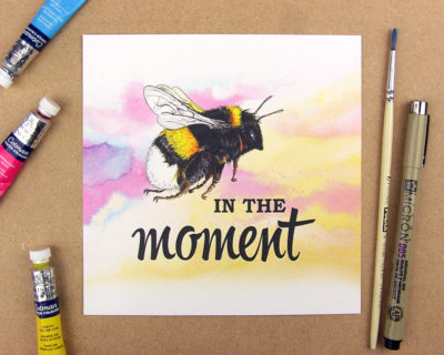 Print showing a bumblebee above the words 'in the moment; on pink and yellow watercolour background. Forming the phrase Be in the moment.