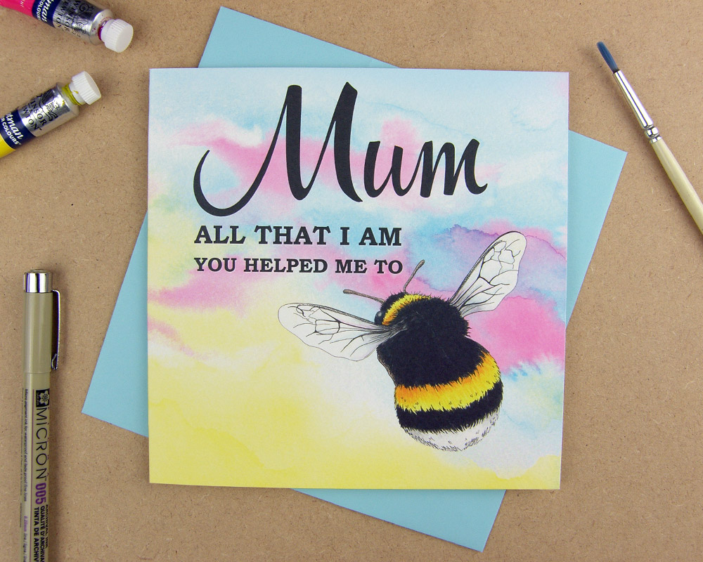 Greetings card with the words 'Mum all that I am you helped me to be' with the word 'be' replaced with an illustrated bumblebee on pink watercolour background