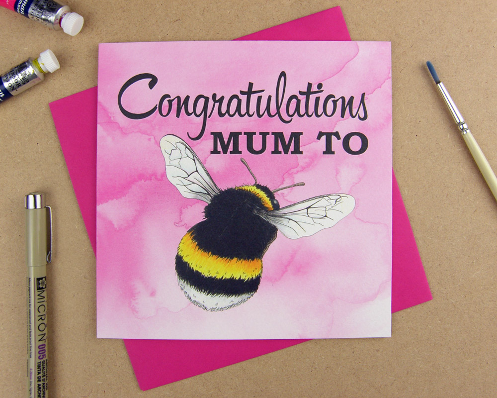 Greetings card with the words 'Congratulations Mum to be' with the word 'be' replaced with an illustrated bumblebee on pink watercolour background