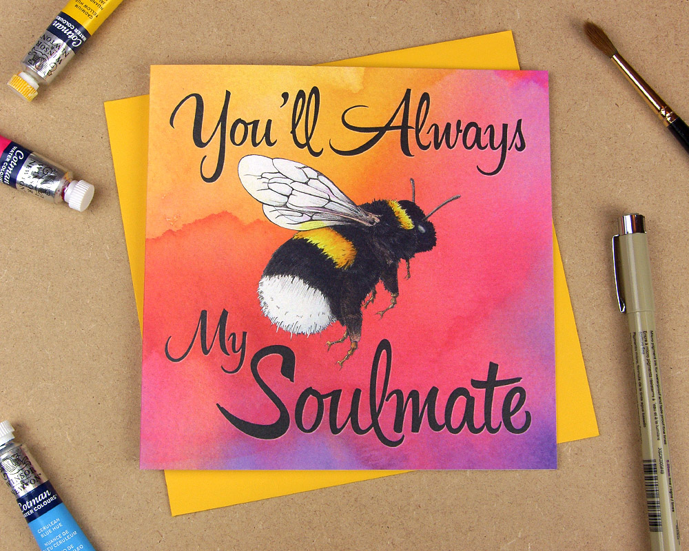 Greetings card with the words 'Be my soulmate' with the word 'be' replaced with an illustrated bumblebee on multi-coloured watercolour background
