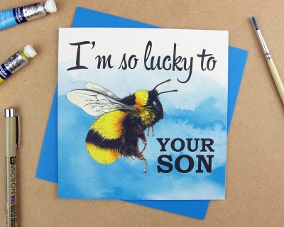 Greetings card with the words 'I'm so lucky to be your son' with the word 'be' replaced with an illustrated bumblebee on pink watercolour background